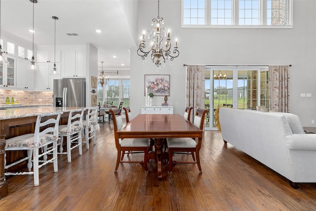 dining room featuring dark wood-type flooring, a wealth of natural light, a chandelier, and a towering ceiling