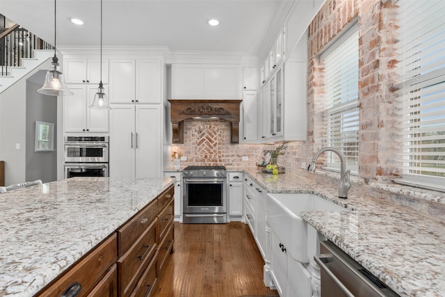 kitchen with sink, white cabinetry, hanging light fixtures, appliances with stainless steel finishes, and light stone countertops