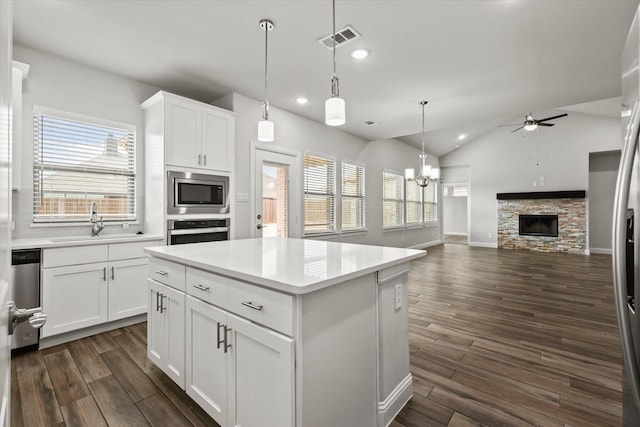 kitchen with appliances with stainless steel finishes, white cabinetry, sink, a kitchen island, and decorative light fixtures