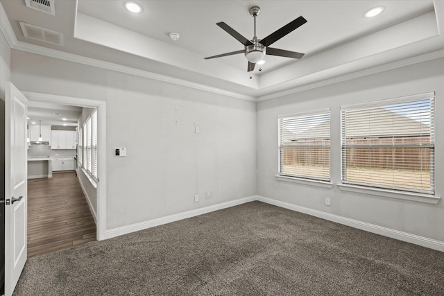 spare room featuring ornamental molding, dark colored carpet, ceiling fan, and a raised ceiling