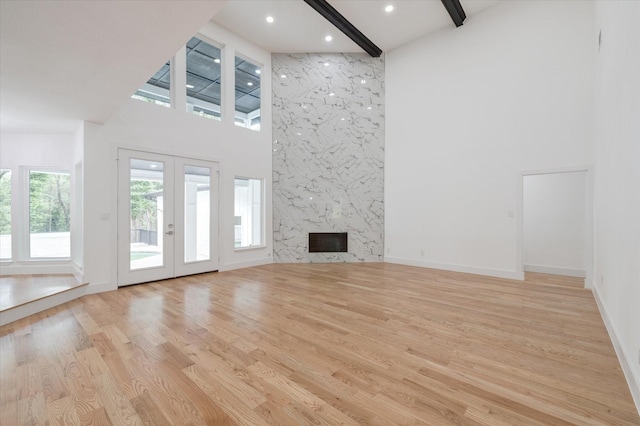 unfurnished living room featuring a high ceiling, a high end fireplace, french doors, beamed ceiling, and light wood-type flooring