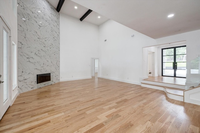 unfurnished living room with light hardwood / wood-style flooring, french doors, beam ceiling, a high ceiling, and a fireplace