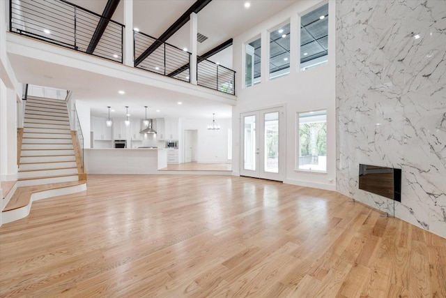 unfurnished living room featuring a premium fireplace, a high ceiling, light hardwood / wood-style flooring, and a notable chandelier