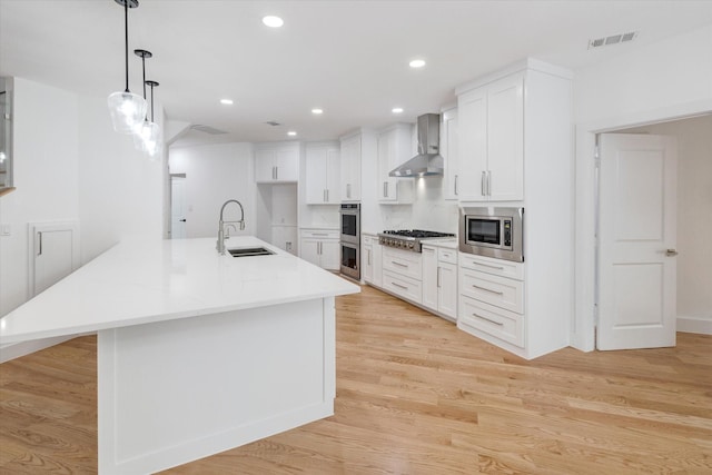 kitchen with sink, decorative light fixtures, white cabinetry, wall chimney range hood, and stainless steel appliances