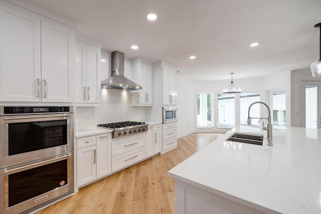 kitchen with wall chimney exhaust hood, white cabinets, decorative light fixtures, and appliances with stainless steel finishes