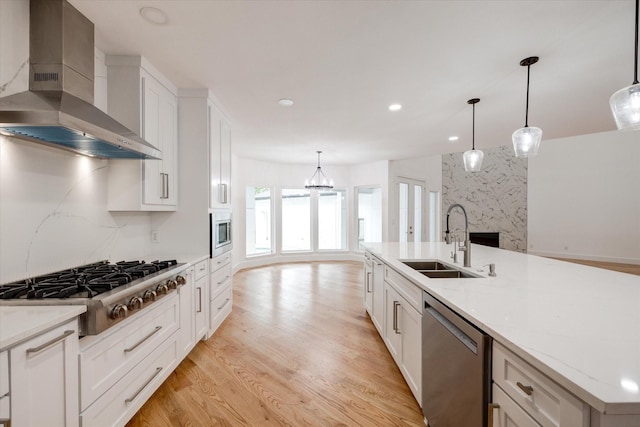 kitchen with a spacious island, wall chimney range hood, stainless steel appliances, sink, and hanging light fixtures