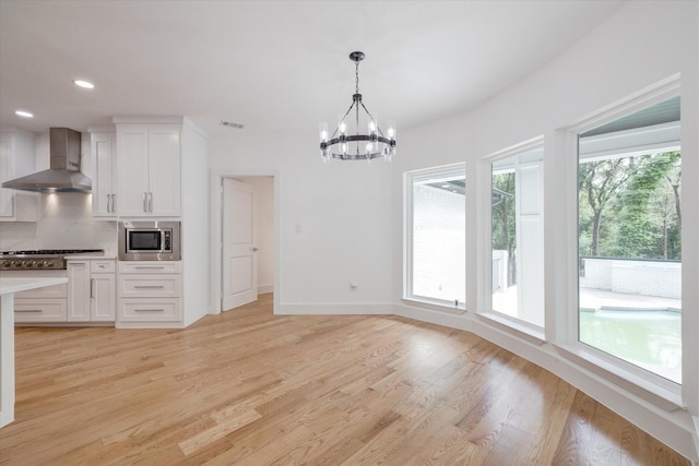 kitchen with white cabinets, appliances with stainless steel finishes, wall chimney exhaust hood, decorative light fixtures, and tasteful backsplash