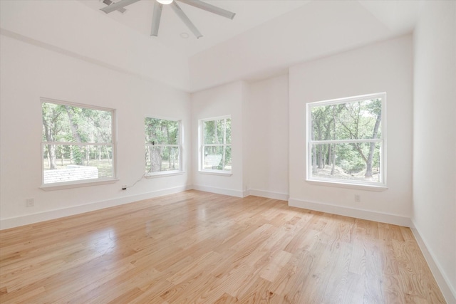 empty room with ceiling fan, a wealth of natural light, a high ceiling, and light hardwood / wood-style floors