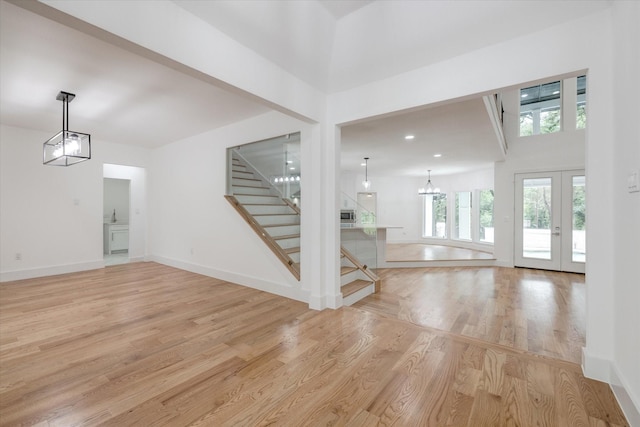 unfurnished living room featuring light hardwood / wood-style floors, a high ceiling, french doors, and a chandelier