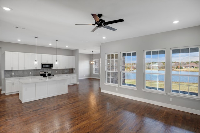 kitchen featuring white cabinets, decorative light fixtures, stainless steel appliances, an island with sink, and decorative backsplash