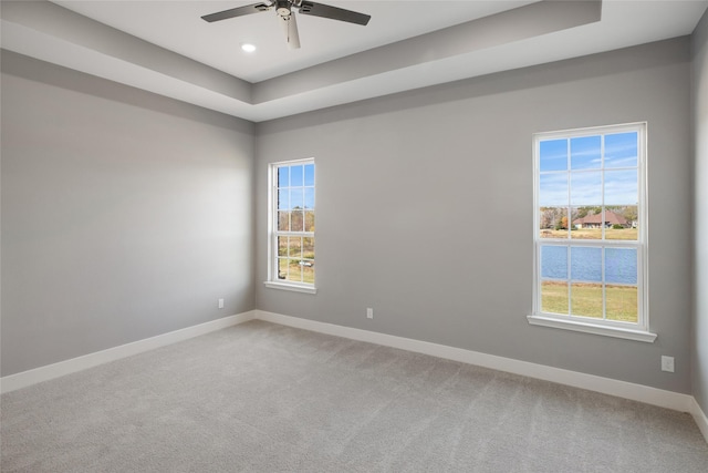 empty room with ceiling fan, plenty of natural light, carpet flooring, and a tray ceiling