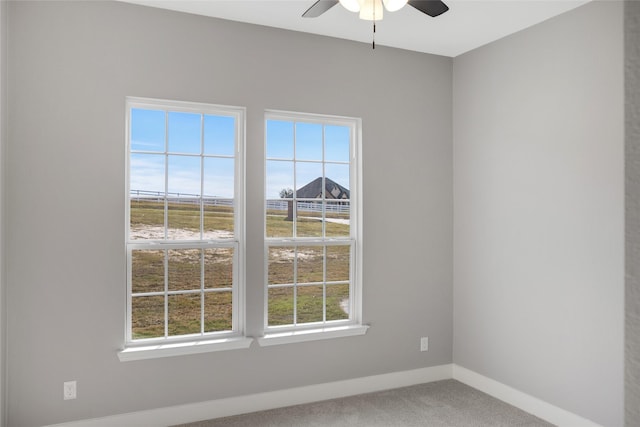 carpeted empty room with a healthy amount of sunlight, ceiling fan, and a raised ceiling