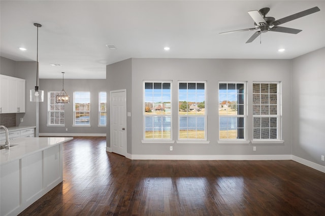 unfurnished living room featuring ceiling fan with notable chandelier, sink, and dark wood-type flooring