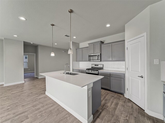 kitchen with appliances with stainless steel finishes, decorative light fixtures, an island with sink, sink, and gray cabinetry