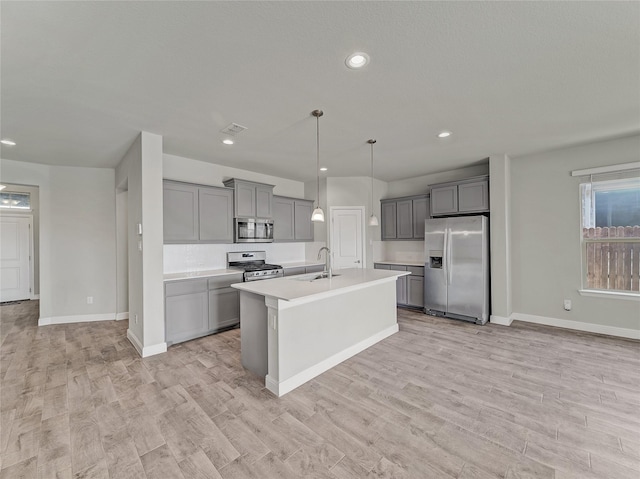 kitchen with gray cabinets, decorative light fixtures, a kitchen island with sink, light hardwood / wood-style floors, and stainless steel appliances