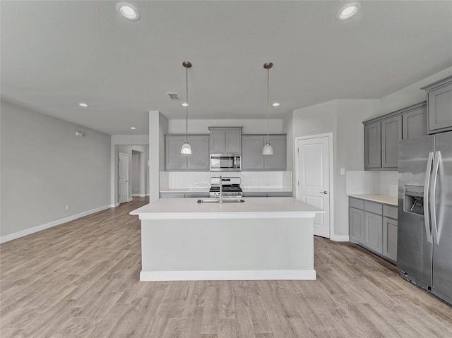 kitchen with appliances with stainless steel finishes, a kitchen island with sink, hanging light fixtures, and backsplash