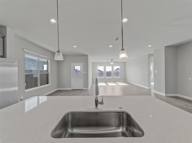 kitchen featuring light stone counters, sink, and hanging light fixtures