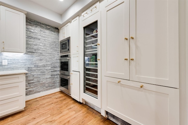 kitchen featuring stainless steel appliances, white cabinetry, beverage cooler, and light hardwood / wood-style floors