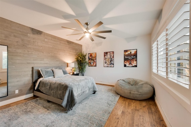 bedroom with ceiling fan, hardwood / wood-style floors, multiple windows, and wood walls