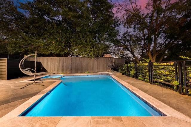 pool at dusk featuring a hot tub and a patio