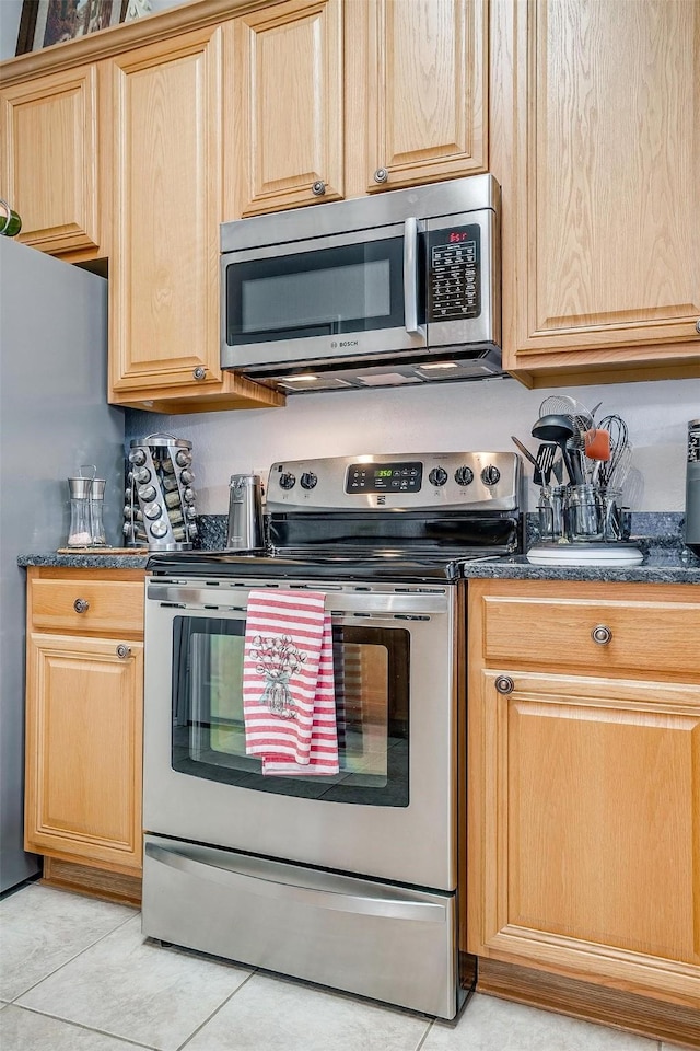 kitchen with stainless steel appliances, dark stone countertops, and light tile patterned floors