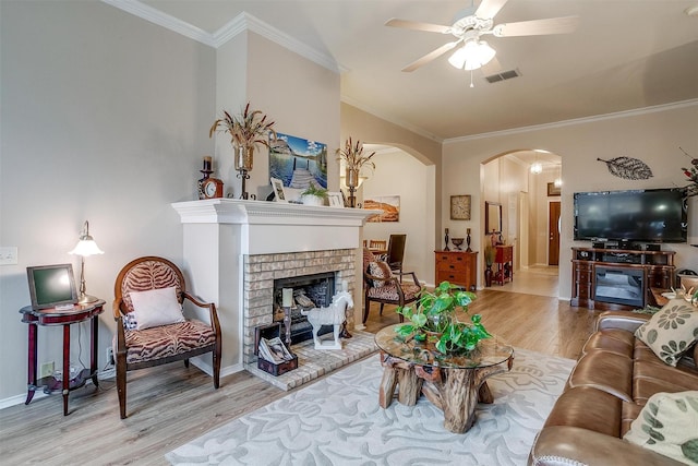 living room with a fireplace, light wood-type flooring, ceiling fan, and ornamental molding