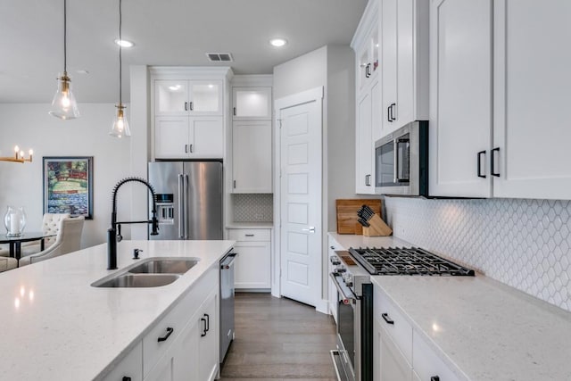 kitchen featuring premium appliances, sink, decorative light fixtures, tasteful backsplash, and white cabinetry