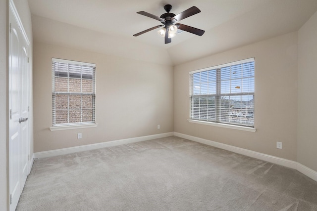 empty room with plenty of natural light, light colored carpet, vaulted ceiling, and ceiling fan