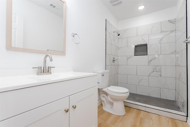 bathroom featuring wood-type flooring, toilet, vanity, and a tile shower