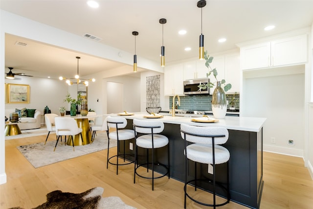 kitchen featuring visible vents, white cabinets, light countertops, backsplash, and stainless steel microwave