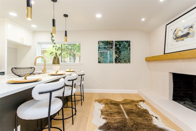 interior space with pendant lighting, white cabinets, light hardwood / wood-style floors, a breakfast bar area, and lofted ceiling