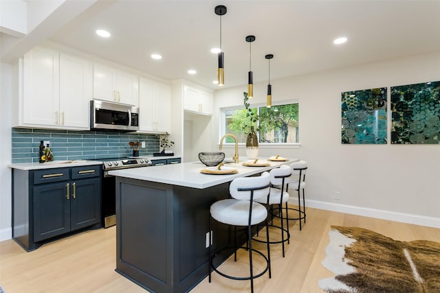 kitchen with light countertops, light wood-style flooring, backsplash, appliances with stainless steel finishes, and white cabinetry