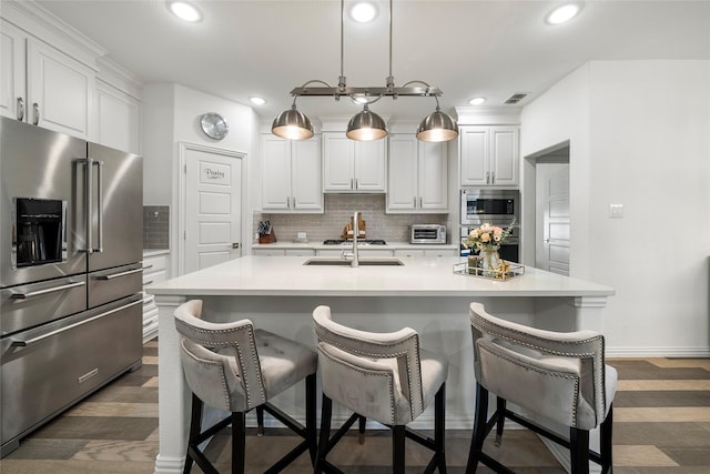 kitchen featuring white cabinets, stainless steel appliances, a kitchen island with sink, and decorative light fixtures