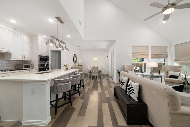 living room with ceiling fan, high vaulted ceiling, sink, and dark hardwood / wood-style flooring