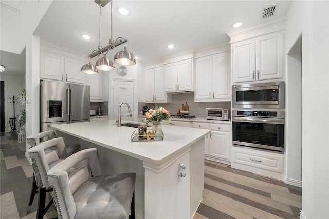 kitchen with a kitchen bar, an island with sink, white cabinets, and appliances with stainless steel finishes