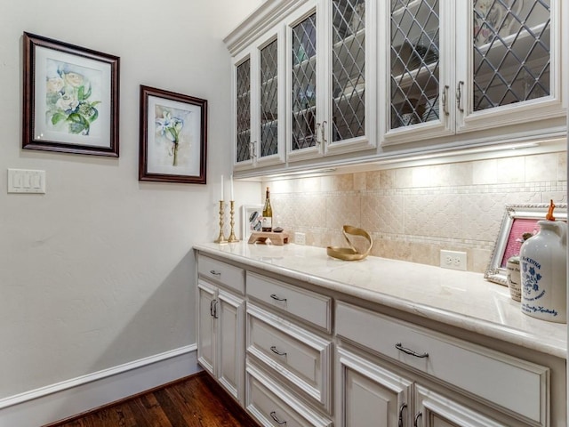 bar featuring backsplash, light stone counters, and dark wood-type flooring