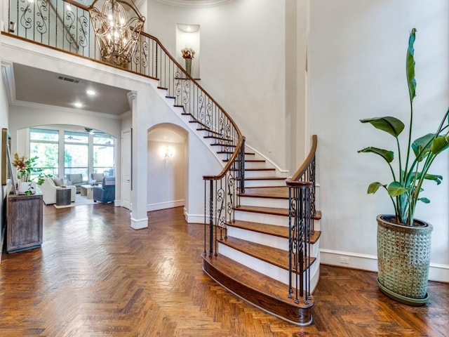 entryway featuring a chandelier, a towering ceiling, dark parquet flooring, and ornamental molding