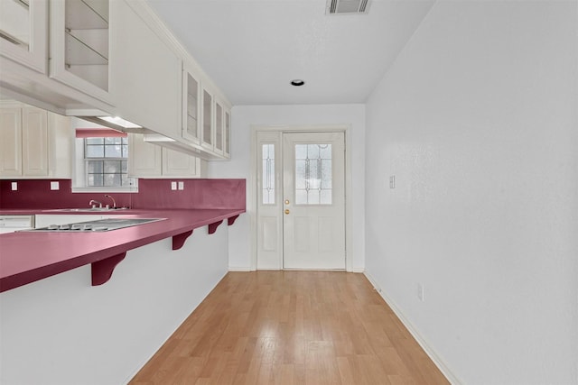 kitchen with stainless steel gas stovetop, white cabinetry, light hardwood / wood-style floors, and a kitchen breakfast bar