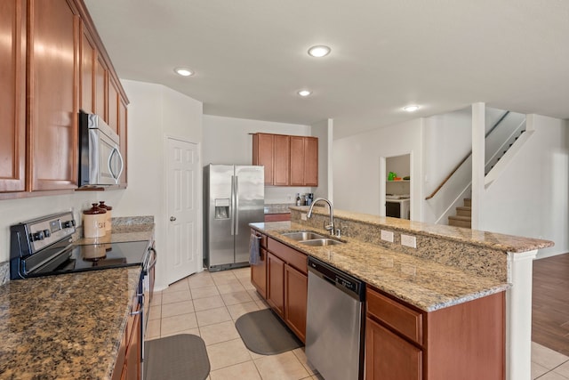 kitchen featuring a center island with sink, washer / clothes dryer, appliances with stainless steel finishes, brown cabinetry, and a sink