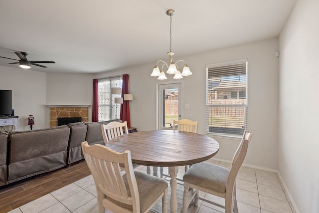 dining space with light wood-style floors, a fireplace, baseboards, and ceiling fan with notable chandelier