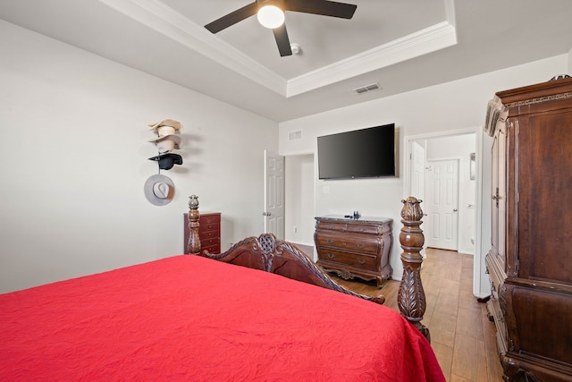 bedroom with ornamental molding, a raised ceiling, visible vents, and wood finished floors