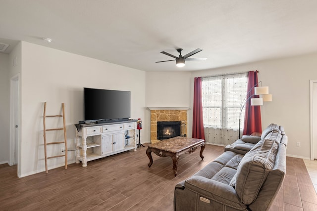 living room with hardwood / wood-style flooring, a stone fireplace, and ceiling fan