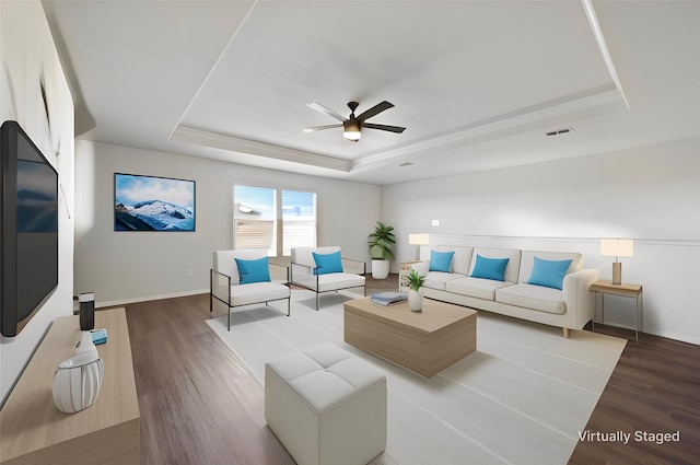 living room with a raised ceiling, visible vents, ceiling fan, and wood finished floors