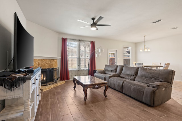 living room with ceiling fan with notable chandelier and a fireplace