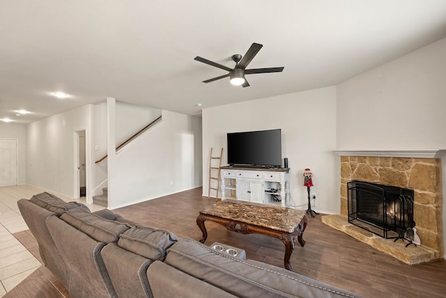 living area with a stone fireplace, wood finished floors, a ceiling fan, baseboards, and stairs