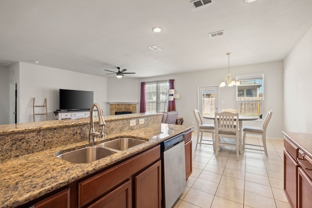 kitchen featuring a stone fireplace, ceiling fan with notable chandelier, a sink, visible vents, and dishwasher