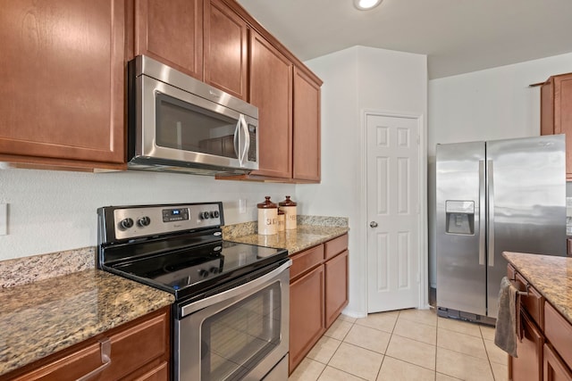 kitchen featuring light tile patterned floors, stainless steel appliances, brown cabinetry, and stone countertops