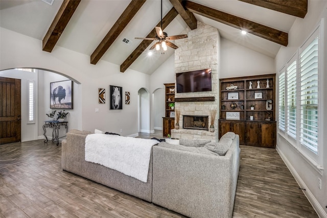 living room with wood-type flooring, a stone fireplace, ceiling fan, high vaulted ceiling, and beam ceiling