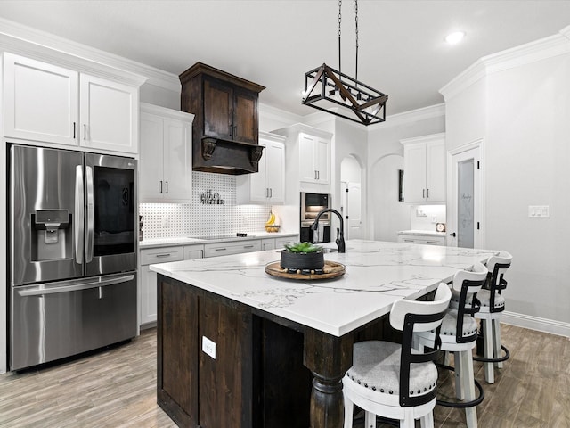 kitchen featuring custom exhaust hood, stainless steel fridge with ice dispenser, a kitchen island with sink, white cabinets, and ornamental molding