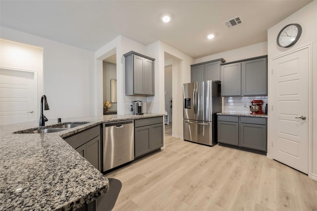 kitchen featuring light stone countertops, sink, light hardwood / wood-style flooring, backsplash, and stainless steel appliances